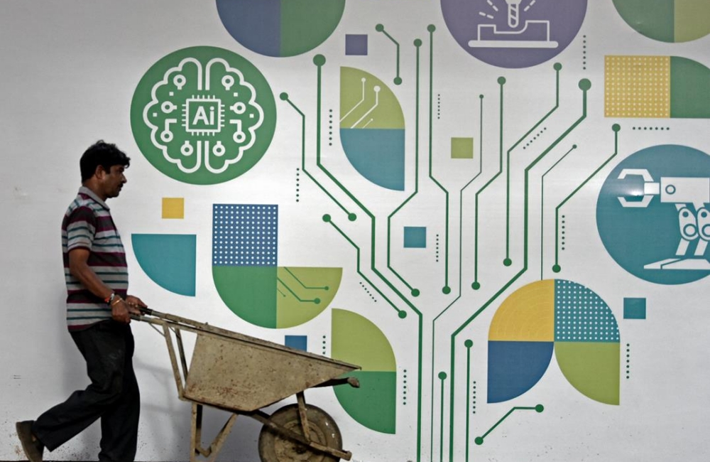 A worker pushes a wheelbarrow trolley and passes by a wall decorated with artificial intelligence signage at Automation Expo 2025 in Mumbai, India, on August 12, 2025. (Photo by Indranil Aditya / NurPhoto / The China-Global South Project )